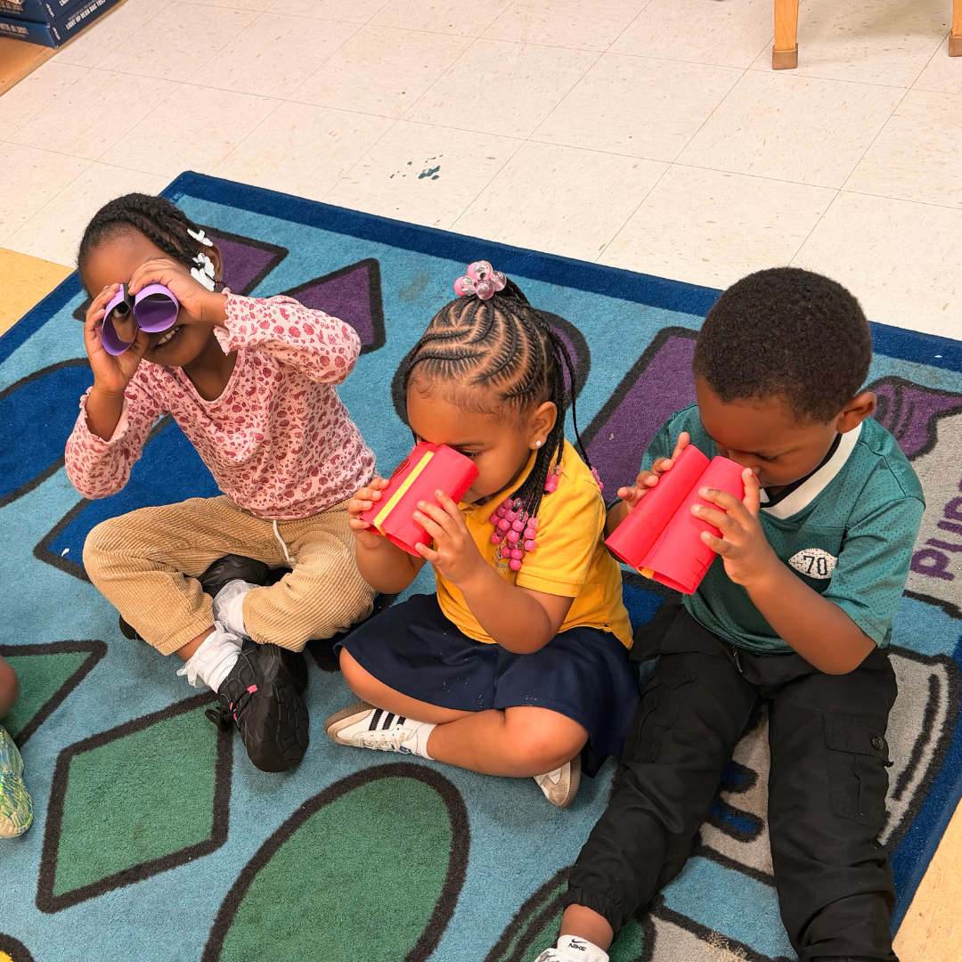 Three scholars playing with colorful handmade paper viewers on our classroom rug